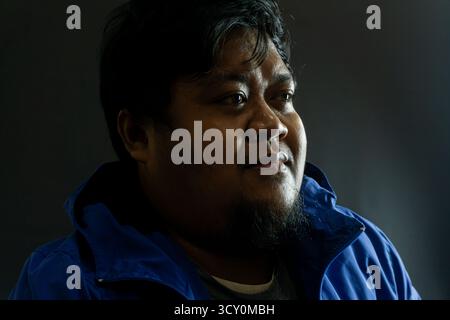 Bearded Indonesian man in his 30s wearing a shiny blue nylon jacket against black background, casual portrait with confident expression and simple lig Stock Photo