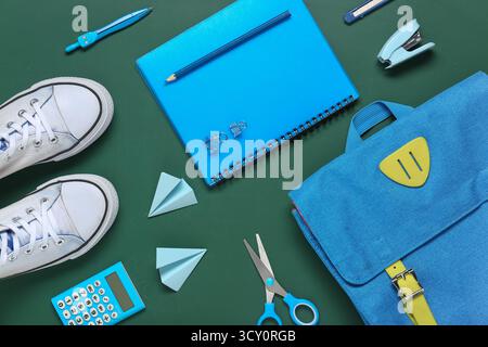 Different stationery with backpack and stylish sneakers on green background Stock Photo