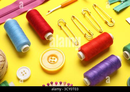 Composition with different thread spools, buttons and pins on yellow background, closeup Stock Photo