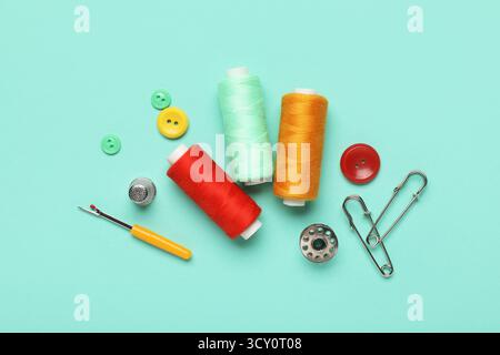 Composition with thread spools, thimble and buttons on mint background Stock Photo