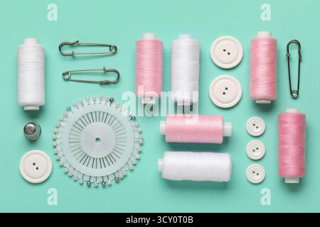 Composition with thread spools, ball pins and buttons on mint background, closeup Stock Photo
