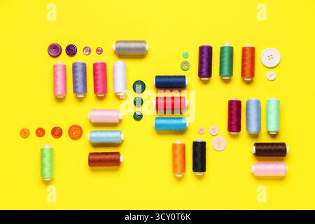 Composition with many different thread spools and buttons on yellow background Stock Photo