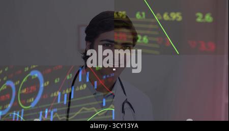 Standing doctor wearing lab coat displaying market data on clinic wall, with stethoscope and graphs Stock Photo