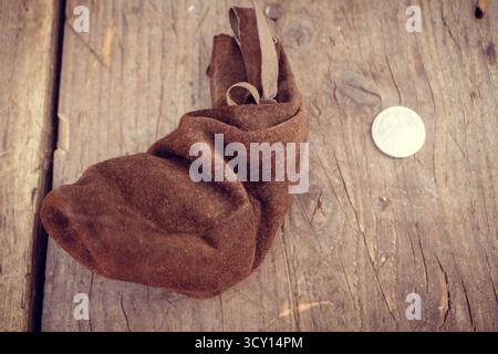 Vintage brown suede pouch with drawstring and coin on rustic wooden table, old style treasure bag, handmade leather accessory, close-up detail Stock Photo