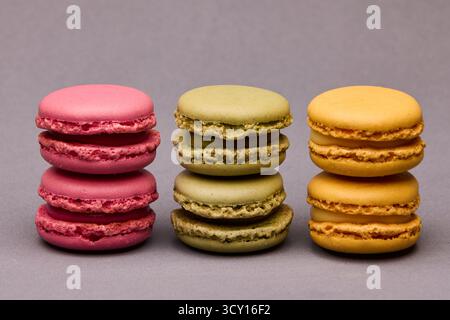 Vertical image of three colorful macarons standing side by side on gray background. Modern patisserie concept and balanced color palette. Stock Photo
