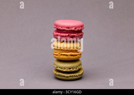 Vertical stack of three colorful macarons in pink, yellow and green on gray background. Studio food photography with modern aesthetic. Stock Photo