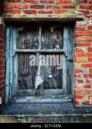 Old brick wall with a weathered wooden window, featuring chipped paint and a torn screen panel, displaying urban decay Stock Photo