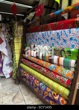 Colorful rolls of vibrant patterned fabric displayed in a market stall with various designs and textures in a street market setting Stock Photo