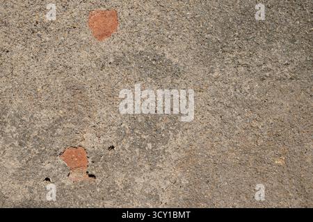 A weathered concrete surface with patches of exposed red material and small holes. Stock Photo