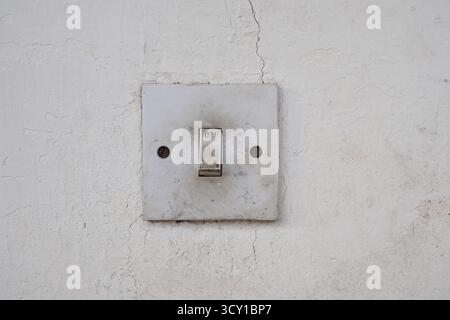 An old, dirty light switch on a cracked white wall Stock Photo