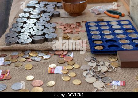 A large collection of old and modern coins on a burlap surface with wooden bowl and keychains for sale at market Stock Photo