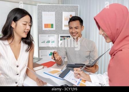 A group of multicultural colleagues in a modern office discussing data and marketing reports. The team focuses on analyzing performance charts and pla Stock Photo