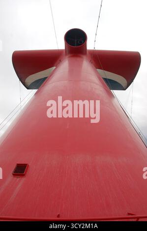 Close-up upward view of a large red cruise ship funnel with white and blue accents, photographed from the deck against a cloudy sky background Stock Photo