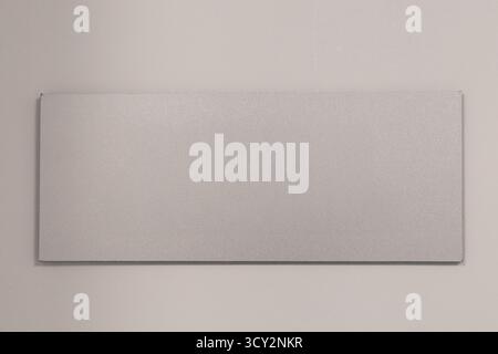 A blank rectangular signboard hangs on a plain wall, emphasizing a minimalistic design Stock Photo