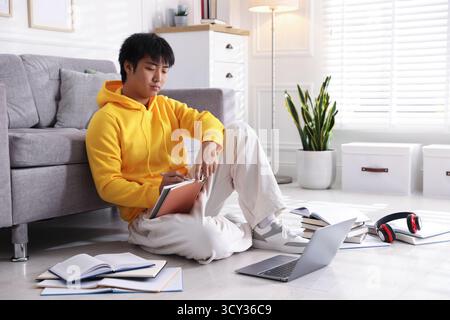 Student with laptop and books preparing for exam on floor at home Stock Photo