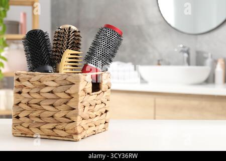 Hair styling. Different combs and brushes in wicker basket on white table in bathroom, closeup. Space for text Stock Photo