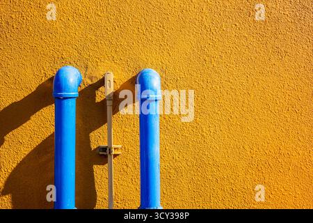 Blue water pipes on yellow textured wall with sunlight shadow, minimal industrial background, colorful contrast for architecture design and creative c Stock Photo