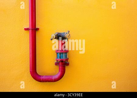 Red fire hydrant pipe on yellow wall background, colorful minimal urban design with bright contrast, architecture detail concept for industrial or cre Stock Photo