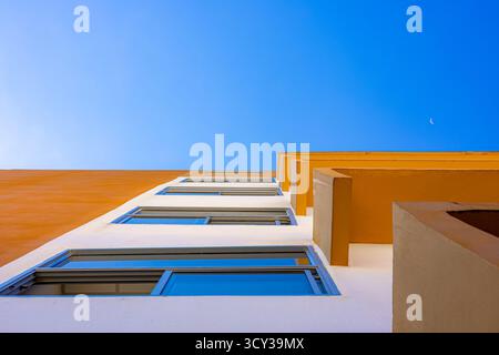 Modern yellow and white building with blue sky view from low angle, minimal architecture perspective with geometric lines and moon in background. Stock Photo