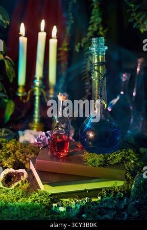 Colorful glass bottles filled with potions rest on a stack of books surrounded by candles and lush greenery. ambiance is magical and inviting, perfect Stock Photo