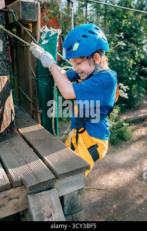 Smiling boy climbing with rope on forest platform, safety harness Stock Photo