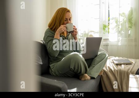 woman enjoying her coffee, while working at laptop from home Stock Photo