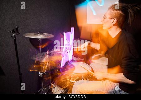 Drummer performing in a vibrant practice studio at night Stock Photo