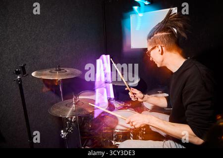 Energetic drummer performing in a studio with vibrant lights Stock Photo