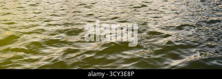 Dark, rippling water sea dramatic. Surface is covered in small waves. Bright, golden-yellow light shines down from left. Water color transitions from Stock Photo
