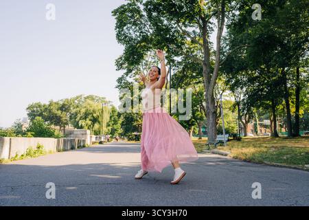 Woman dancing happily in park wearing pink skirt Stock Photo