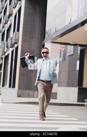 Businessman in a stylish blazer celebrates success as he crosses a busy city street with a briefcase in hand Stock Photo