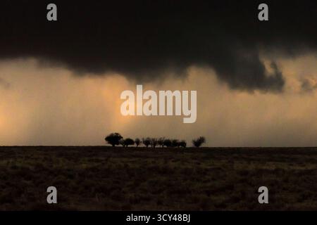 A distant tornado spins beneath dark, menacing storm clouds over a dusty rural road, capturing nature’s fury, dramatic skies, extreme weather Stock Photo