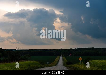 Country road fades into the distance beneath dark, moving clouds, a dramatic sky textured with grey and shadow, evoking moody atmosphere, beauty Stock Photo