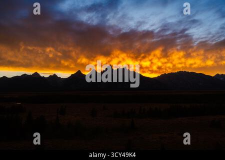 Fiery colorful sky glows with beauty over silhouette mountains, creating a dramatic scene with vibrant clouds, shadow, and texture Stock Photo