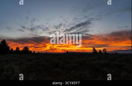 Bright orange and red sunrise colors fill moving clouds, creating a dramatic sky with soft texture and shadow, showcasing the colorful tranquil beauty Stock Photo
