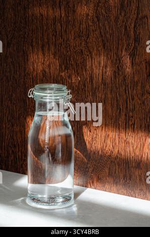 Glass carafe with water on stone countertop in dark wood kitchen with sunlight. Drink more water. Ideal for wellness, design and lifestyle marketing. Stock Photo