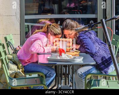 Two young women viewing a smartphone or tablet whilst shading sunlight from it - Tours, Indre-et-Loire (37), France. Stock Photo