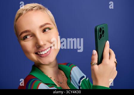 Stylish young woman beams at camera, showcasing her trendy outfit and bright phone case. Stock Photo