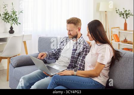 Married couple sitting on the couch at home and using a laptop computer together Stock Photo