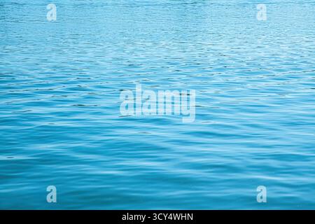 The smooth surface of a river reflects a variety of blue shades as gentle ripples create a serene atmosphere. Sunlight casts a soft glow, enhancing th Stock Photo