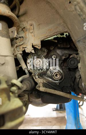 A close-up shot of a dirty and oily car engine, showing the timing belt and pulleys, as seen from underneath a vehicle during maintenance or repair. Stock Photo