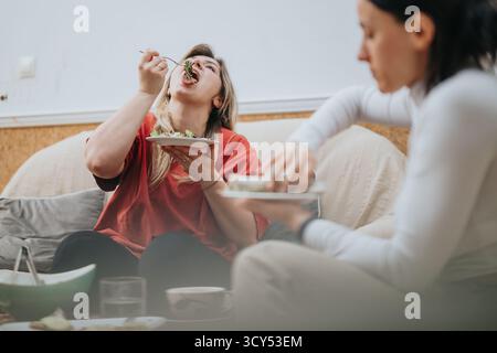 Two female friends enjoying a meal together and laughing indoors Stock Photo