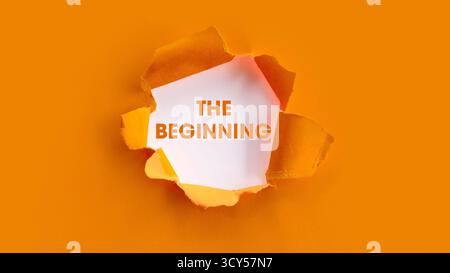 The Inspirational Phrase THE BEGINNING Revealed through a Circular Rip in a Vibrant Orange Paper Background, Symbolizing a Fresh Start and New Project Stock Photo