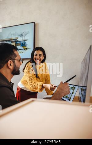 Two architects collaborating on a project in a modern office, featuring a smiling woman wearing a yellow sweater and a man holding a pen, discussing d Stock Photo