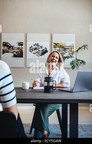 A smiling woman is seen discussing projects during a casual meeting in an architecture office, showcasing creativity and teamwork in a modern workspac Stock Photo