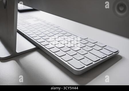 Wireless Apple keyboard connected to an Apple iMac computer sitting on a white desk Stock Photo