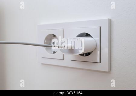 USB charging cord inserted into a wall power socket Stock Photo