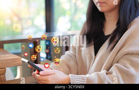 Engaging with social media on the phone. Woman use a smartphone, with social media reactions and emojis floating around, representing online interacti Stock Photo