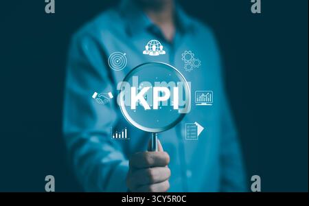 Businessman analyzing key performance indicators (KPI). Business executive holding a magnifying glass focused on KPI and related business symbols. Stock Photo
