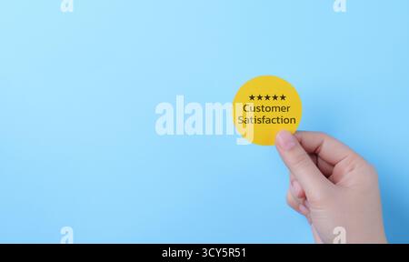 Customer review satisfaction feedback survey concept. Hand holding five-star customer satisfaction rating on a blue background, Stock Photo